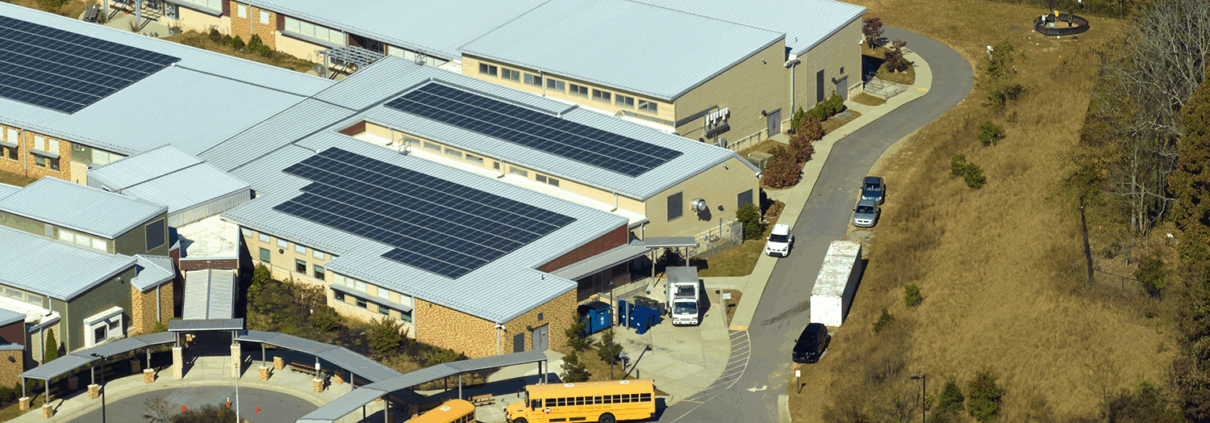 Aerial view of a high school in Pennsylvania with rooftop solar panels installed by Canopy Solar, surrounded by sports fields, school buses, and green landscaping on a sunny day